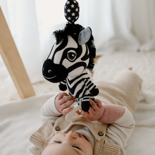 Load image into Gallery viewer, Baby lying on a soft play mat holding Ziggy the Zebra — a high-contrast black and white sensory toy with crinkly features and a teething ring, designed by Young Wonderer