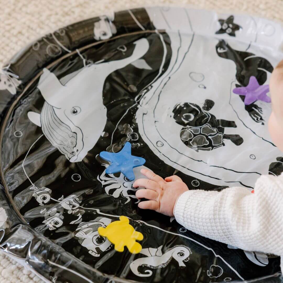 Baby reaching for colourful sea creatures on Young Wonderer's black and white high contrast Under the Sea Sensory Water Mat